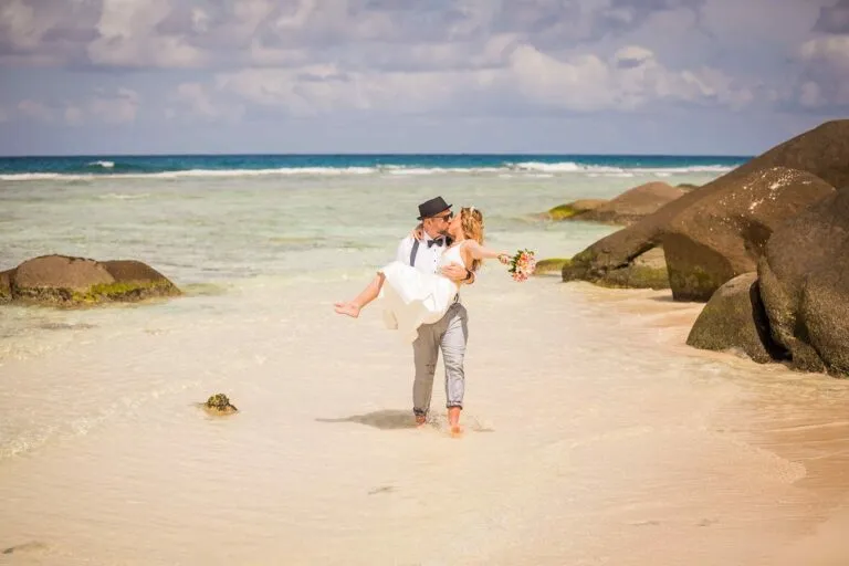 Agnes & Tom – groom carrying the bride on a sandy beach next to granite boulders