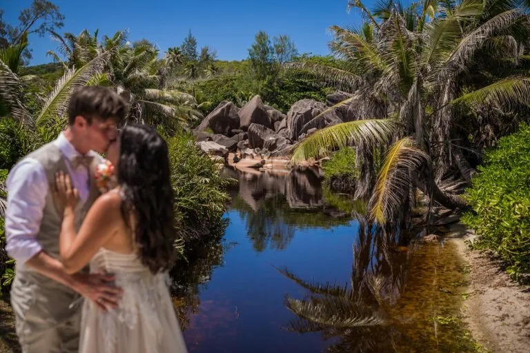 Nicole & Benjamin – couple kissing beside a lagoon framed by palm trees and granite rocks